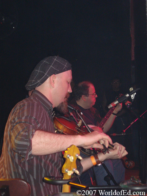 Two men sitting on stage playing instruments.