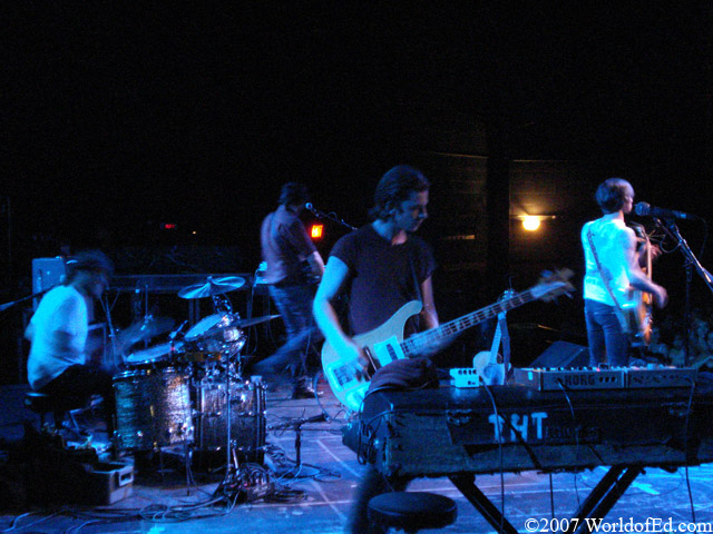 Aaron playing bass in the foreground with the band in the background.