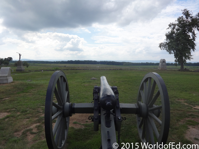 A view of a large field from behind a cannon.