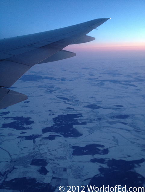 A plane wing while flying over Europe that is covered in snow.